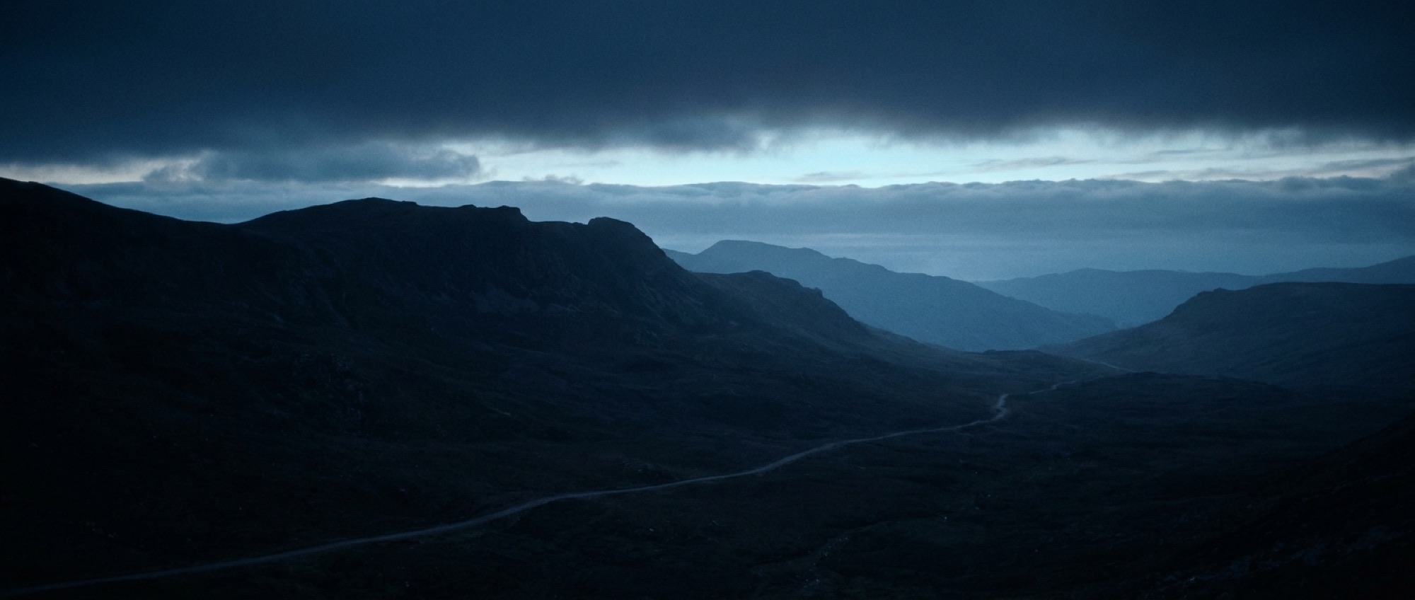 Dusk over remote highlands, a faint track winding beyond the ridgeline